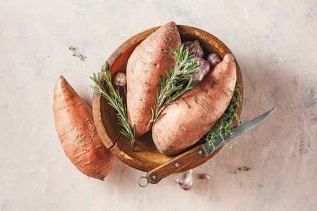 Sweet potatoes in a large wooden bowl with rosemary and garlic.の写真素材