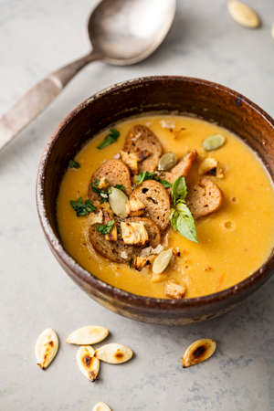 Pumpkin soup in a bowl garnished with pumpkin seed and croutons, close-up.の写真素材