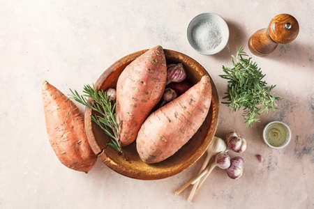Sweet potatoes in a large wooden bowl with rosemary and garlic, top view.の写真素材
