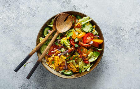 Vegetable salad with tomatoes, lettuce, cucumbers, onions and grilled corn, top view.の写真素材