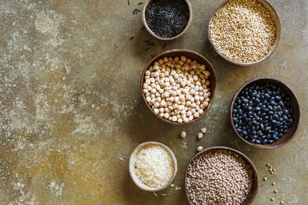 Different types of beans and rice in coconut bowls, on a brown background with copy space, top view.の写真素材