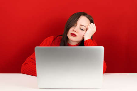 beautiful girl is sad at the computer on a red backgroundの写真素材