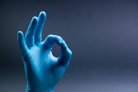 Ok sign is showed by right man hand in a blue medical glove on a black background. Okay. All rightの写真素材