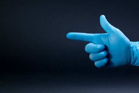 A gun sign by right man hand in a blue medical glove on a black backgroundの写真素材
