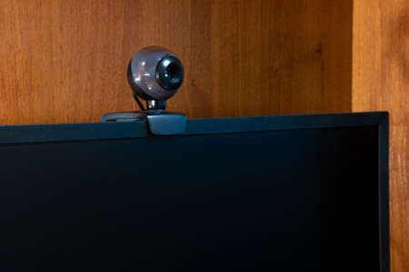 External round black web camera on a black monitor. Webcam on a wooden background.
