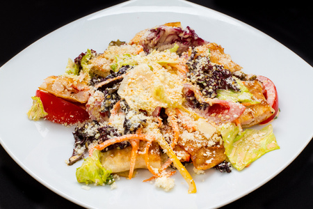 warm salad with cheese, fish, vegetables on a white plate, black backgroundの写真素材