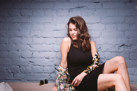 sexy beautiful girl in black dress on sofa. Brick, blue backgroundの写真素材