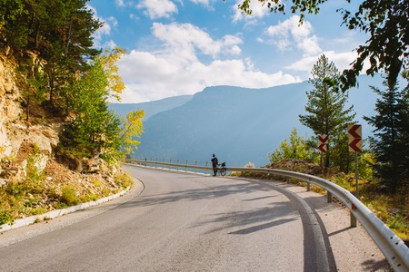 A man stands next to a Bicycle on the paved mountain road. Summer in the mountains of Bulgariaの写真素材