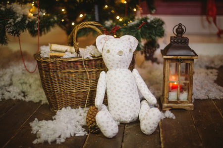 Teddy bear gift sitting under decorated with lights Christmas tree with gift boxesの写真素材