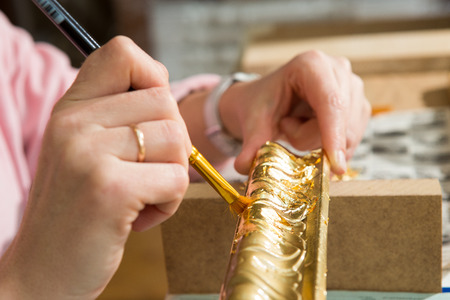 female hand painting with a brush baguette for ceiling and walls in gold colorの写真素材