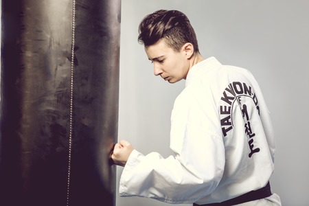 girl in a white kimono beats black punching bag isolated on grey background. Of Tae Kwon do, karate, kickの写真素材