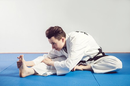 girl in karate suit kimono in studio at grey background. Female child shows judo or karate stans in...