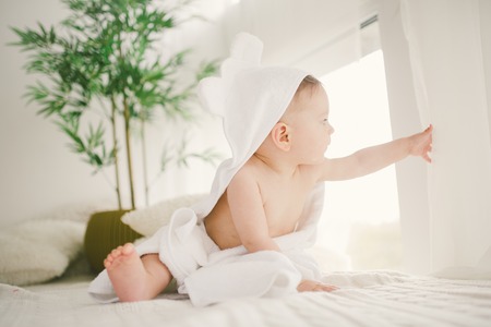 beautiful smiling newborn baby boy covered with white bamboo towel with fun ears. Sitting on a white knit, wool plaid bright interior. The natural light from the window. bamboo, wood, potの写真素材