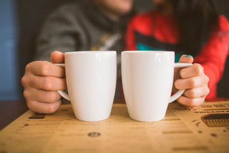 Lovely sweet couple kisses in the background. Pair holds in their hands cups of coffee wite colorの写真素材