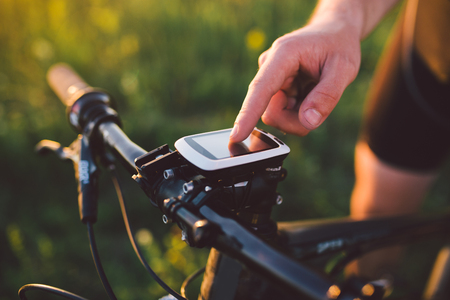 A young brunette guy on a mountain bike uses a cycling computer, a navigator in the field at sunset of the dayの写真素材