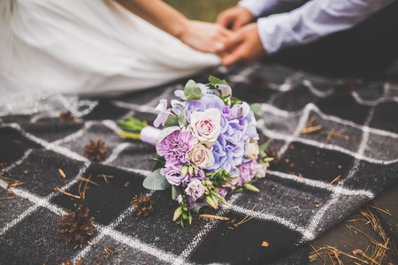 Enamored bride and groom are sitting on a plaid plaid holding hands. A wedding bouquet lies nearbyの写真素材
