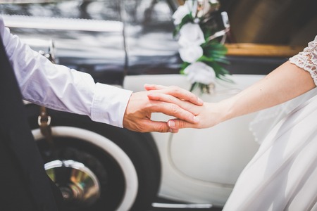 The bride and groom hold hands near the retro carの写真素材