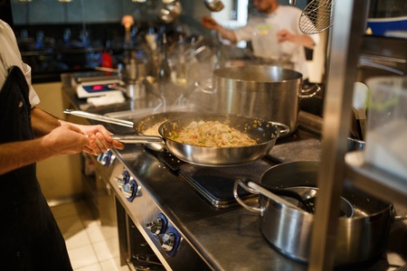 The man cook prepares rice, risotto in a large frying pan in the kitchen of the restaurantの写真素材
