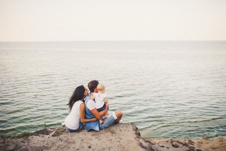 A young family of three, Mom, Dad and daughter spend one year on a high cliff looking at the sea in summer. They are dressed in junior jackets and white T-shirtsの写真素材