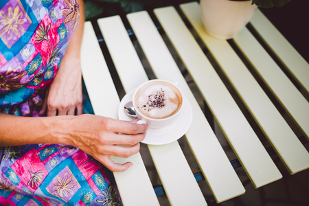 Close up image of woman shaking her favorite tasty chocolate cappuccino at cute cafeteria, wearing retro white skirt and accessorizes. Shabby chic style.の写真素材