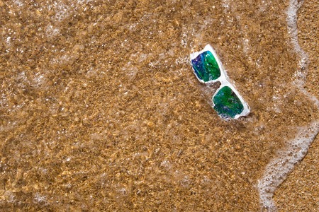 sunglasses with a white rim and mirror lenses in the sea water covered with a wave on the yellow...