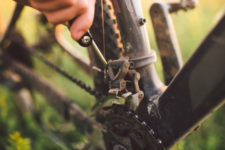 hand with a bicycle tool was engaged in fixing a bicycle outdoors at sunset close-up