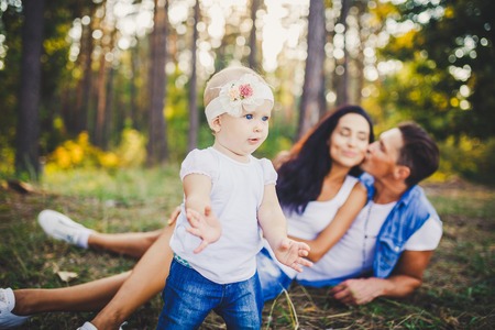 little girl one year on the background of parents resting lying on grass learning to walk on nature...