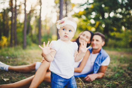 little girl one year on the background of parents resting lying on grass learning to walk on nature in the park. The first steps of a child in nature outside the city in the forestの写真素材