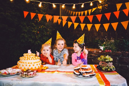 Childrens birthday party. Three cheerful children girls eating cake with their hands and smearing...