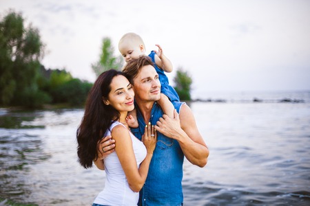 beautiful young family on vacation with baby. The father holds the blonde girl in her arms, and the brunette's mother hugs her husband. The concept of a family beach holiday summer near the sea.の写真素材