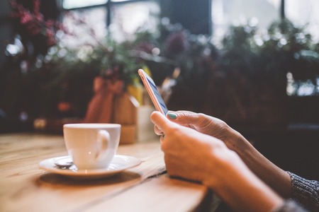 hands close-up of a beautiful young girl uses,types text on mobile phone at a wooden table near a...