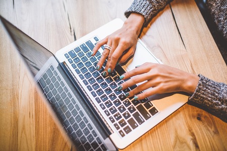 Close-up of the hand of a young girl in a gray sweater use laptop technology on a wooden table in a cafe in the winter. Near the mobile phone and glasses. The concept of remote work business lady.の写真素材