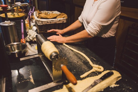 The hands of a female baker are cooking trdelnik or Trdlo in a cozy city cafe a national treat in the Czech Republic in the winter.の写真素材