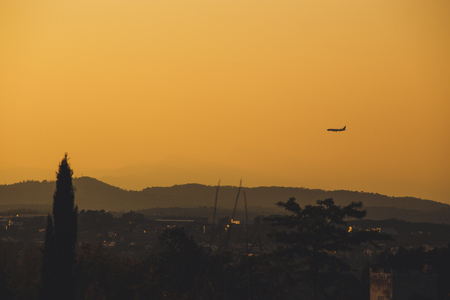 the silhouette of the passenger airplane at sunset bright orange sky, mountains and southern trees in Spain is not near the city of Girona.の写真素材