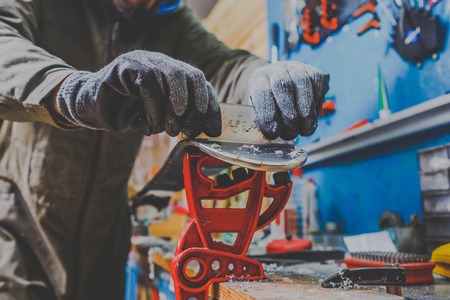 A male worker in a ski service workshop repairs the sliding surface of the skis. Close-up of a hand with a plastic scrapper for removing wax, removing new wax. Theme repair of ski curb.の写真素材