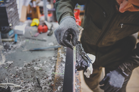 A man repairman in workshop ski service repairing the sliding surface of the ski at Ski vise. In hands of instrument Final edge sharping by gummy stone. Theme ski repair and maintenance of equipment.の写真素材