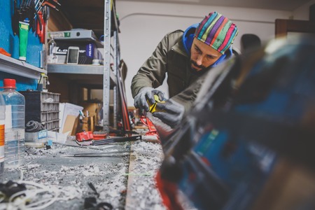 Male worker repairing Stone, edge sharpening in ski service workshop, sliding surface of the skis. sharpening of an edging of a mountain skis by means of the individual tool. Theme repair of ski curb.の写真素材