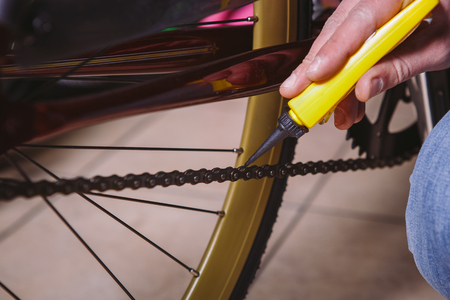 Theme repair bikes. Close-up of a Caucasian man's hand use a Chain Lubricant in a yellow lubricator for llubricator a bicycle chain on a red bicycle.の写真素材