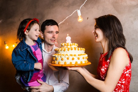 Theme family holiday childrens birthday and blowing out candles on large cake. young family of three...