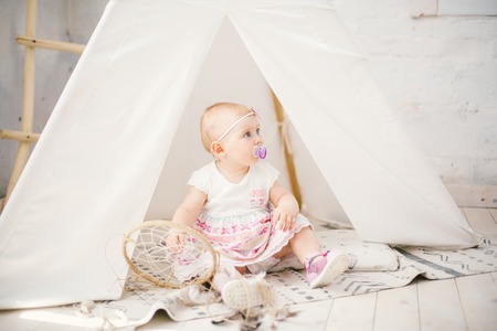 Amulet dream catcher and little baby girl one year with blue eyes, blonde sits on the floor in a dress and holds an Indian amulet, amulet for a good sleep. Summer in sunny weather.の写真素材