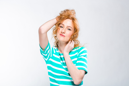 Close-up portrait of a young, beautiful woman with red curly hair in a summer dress with strips of blue in the studio on a gray background. Theme of summer vacation, tourism and summer clothes.の写真素材