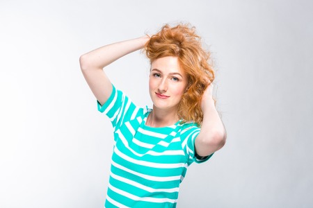 Close-up portrait of a young, beautiful woman with red curly hair in a summer dress with strips of...