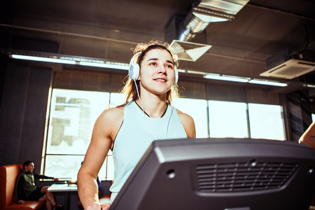 Theme is sport and music. A beautiful inflated Caucasian woman running in a gym on a treadmill. On...