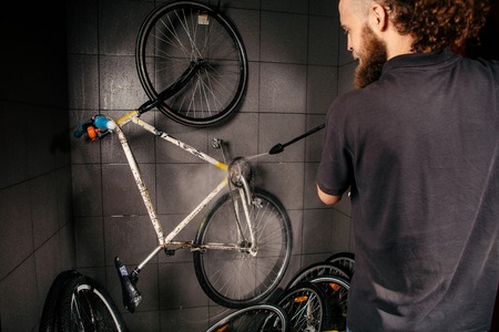 Services professional washing of a bicycle in the workshop. Close-up of hand Young Caucasian stylish man doing bicycle cleaning using automatic electric water pump. Sprays scatter from the pressure.の写真素材