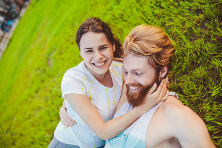 Theme is sport and a healthy lifestyle. A young man and woman couple are resting lying on their backs on the green grass, a lawn in a pack after playing sports. Joint training of the family.の写真素材