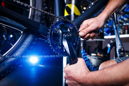 A close-up of a male bicycle mechanic's hand in the workshop uses a screwdriver tool to adjust and...