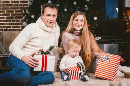 Family three Caucasian people sitting under coniferous tree Christmas tree on floor of carpet wool.