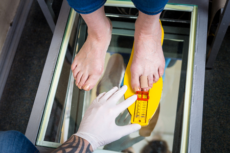 Orthopedics and medicine. Young Caucasian doctor hands man tattoo latex gloves size measurement shape of the foot for the manufacture of individual orthopedic insole. Flatfoot and foot diseases.の写真素材