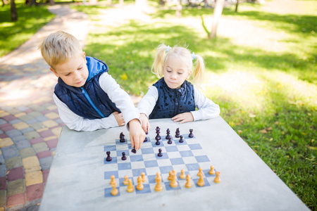 The topic children learning, logical development, mind and math, miscalculation moves advance. large family brothers and sister Caucasian boys and girl playing chess park bright sunny weather autumn.の写真素材