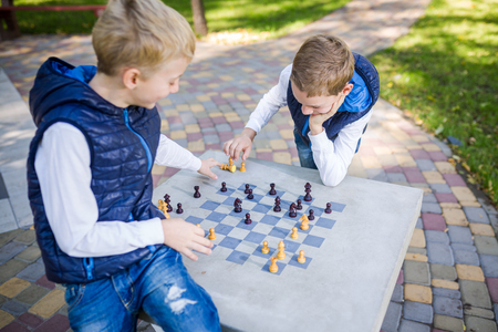 The topic is children learning, logical development, mind math, miscalculation moves advance. Big family two brothers Caucasian boys playing chess in the park in bright sunny weather in the autumn.の写真素材